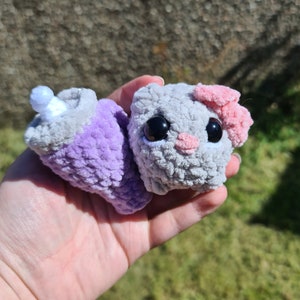 Sad hamster as featured on TikTok meme videos. Silver in colour with large black eyes, pink nose and pink bow on its ear. It have a crochet Stanley cup keyring in purple beside it