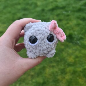 Viral sad hamster crochet cuddly toy made in fluffy grey yarn with large safety eyes and a pink bow