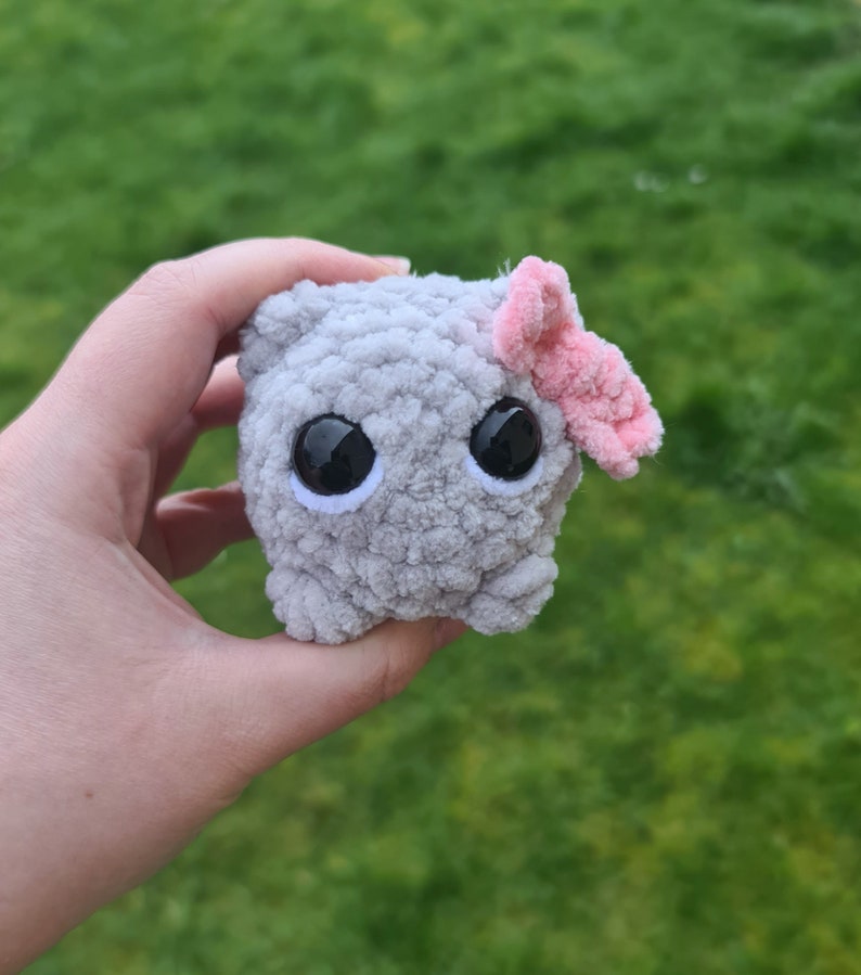 Viral sad hamster crochet cuddly toy made in fluffy grey yarn with large safety eyes and a pink bow