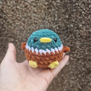 Mini crochet mallard duck plush toy sitting in palm for scale