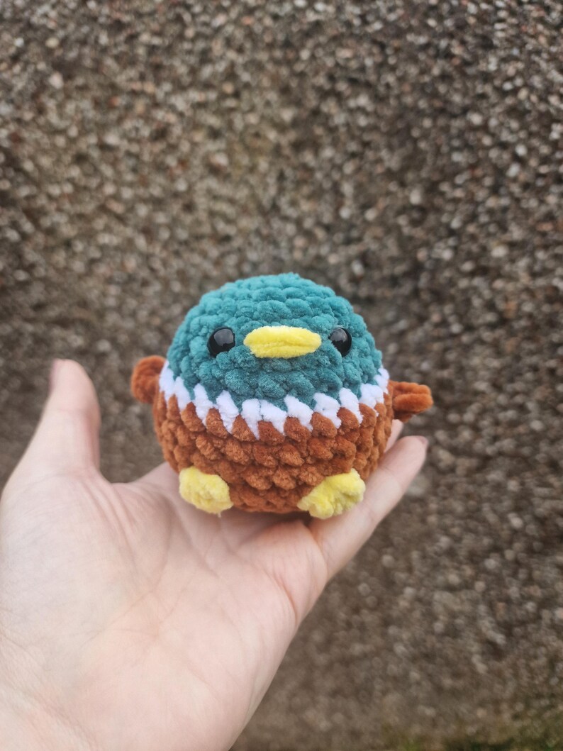 Mini crochet mallard duck plush toy sitting in palm for scale