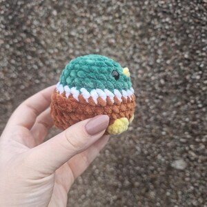 Small amigurumi mallard duck plush toy held against textured background