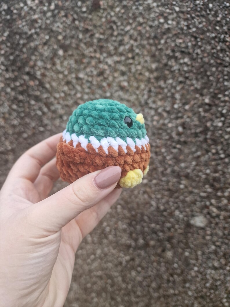 Small amigurumi mallard duck plush toy held against textured background