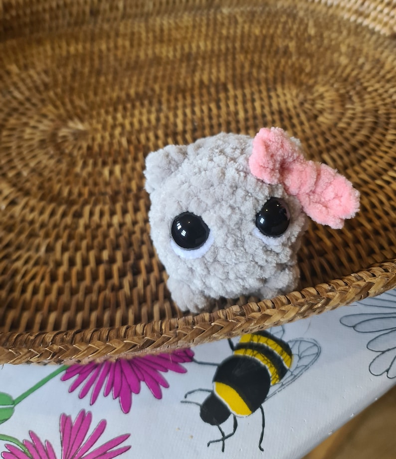 Viral sad hamster crochet cuddly toy made in fluffy grey yarn with large safety eyes and a pink bow