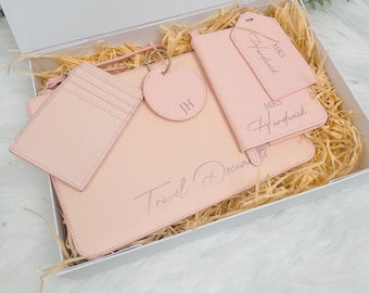 Puede incluir: Un set de regalo de artículos esenciales para viajes de color rosa en una caja blanca con un portapasaporte rosa, una etiqueta de equipaje, un porta tarjetas y un llavero con las iniciales "JH" y el texto "Documentos de viaje".