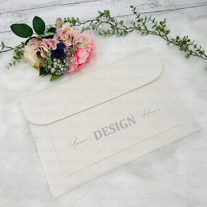 Könnte beinhalten: Ein weißer Umschlag mit einer Klappe oben. Der Umschlag hat ein graues Design mit der Aufschrift "Your Design Here" und einer handschriftlichen Unterschrift darunter. Der Umschlag liegt auf einer weißen Oberfläche mit einem Strauß rosa Blumen im Hintergrund.