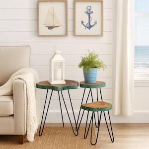 May include: Three wooden side tables with black hairpin legs. The tables have a natural wood top with a green edge. A white lantern with a candle and a blue pot with a plant are on the tables. Two framed nautical prints hang on the wall.