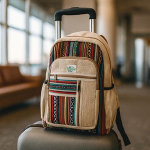 May include: Beige backpack with colourful woven fabric accents. The backpack has a front pocket with a zip and a small patch that says "Himalayan". The backpack is on top of a rolling suitcase.