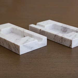 Op de afbeelding: Twee rechthoekige trays van wit marmer met grijze aderen. Elke tray heeft een uitgeholde groef in het midden.