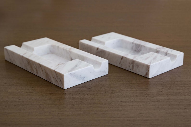 Op de afbeelding: Twee rechthoekige trays van wit marmer met grijze aderen. Elke tray heeft een uitgeholde groef in het midden.