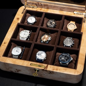 May include: A wooden watch box with a hinged lid, open to reveal nine compartments lined with brown velvet. Each compartment holds a different wristwatch with various styles and colors.