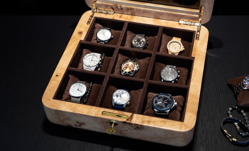 May include: A wooden watch box with a hinged lid, open to reveal nine compartments lined with brown velvet. Each compartment holds a different wristwatch with various styles and colors.