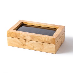 Pu&ograve; includere: Una scatola porta orologi in legno con un coperchio in vetro. La scatola ha una venatura del legno di colore marrone chiaro ed &egrave; composta da due pezzi. Il pezzo superiore ha una finestra in vetro che mostra l'interno della scatola. La scatola &egrave; vuota.