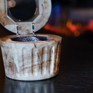 May include: A wooden watch box with a hinged lid and a watch inside. The box is made of light wood with a natural grain pattern. The lid is open and the watch is visible inside.
