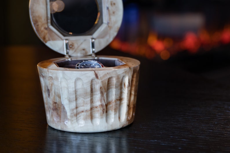 May include: A wooden watch box with a hinged lid and a watch inside. The box is made of light wood with a natural grain pattern. The lid is open and the watch is visible inside.
