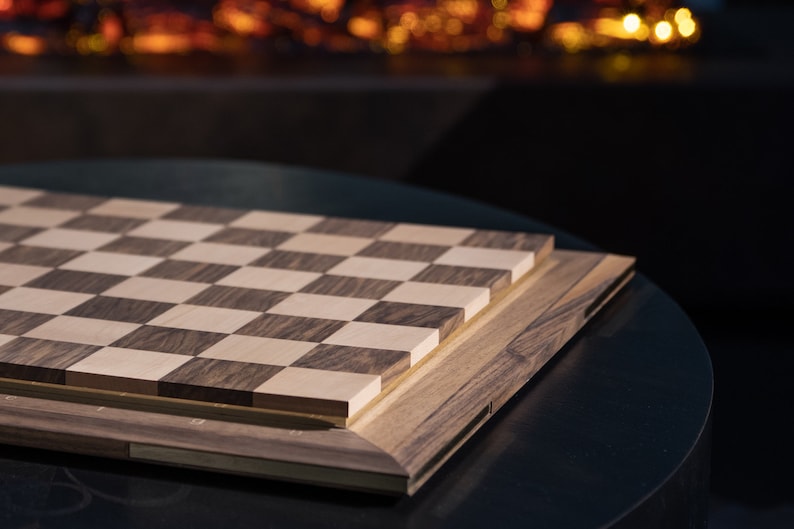 May include: A wooden chessboard with a dark brown and light wood checkered pattern. The board is closed and sitting on a black surface.