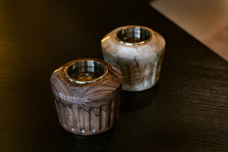 May include: Two wooden incense burners with brass accents. One is brown with a wood grain pattern and the other is white with a marbled pattern.