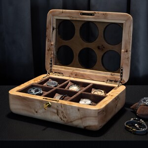 May include: A wooden watch box with a glass top and eight compartments for storing watches. The box is open and has several watches inside.