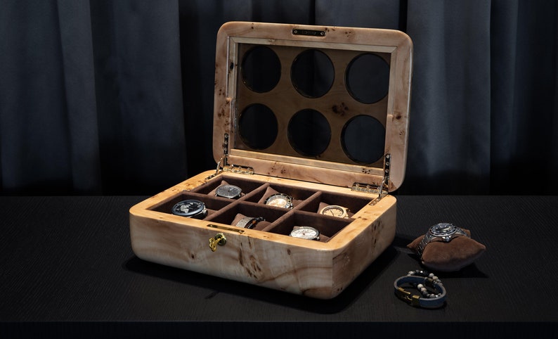 May include: A wooden watch box with a glass top and eight compartments for storing watches. The box is open and has several watches inside.