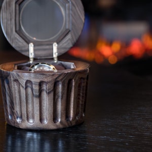 May include: A dark wood watch box with a hinged lid and a watch inside. The box has a fluted design and is open.
