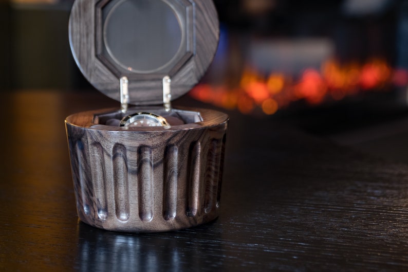 May include: A dark wood watch box with a hinged lid and a watch inside. The box has a fluted design and is open.