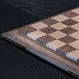 May include: A wooden chessboard with a dark brown and light wood pattern. The board is made of two layers of wood, with the top layer being the playing surface. The board is labelled with letters and numbers along the edges.