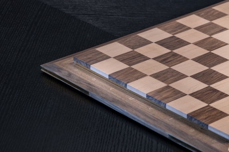 May include: A wooden chessboard with a dark brown and light wood pattern. The board is made of two layers of wood, with the top layer being the playing surface. The board is labelled with letters and numbers along the edges.