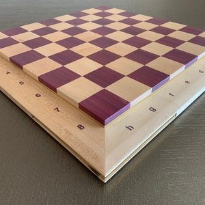 Puede incluir: Un tablero de ajedrez de madera con un marco marr&oacute;n claro y un patr&oacute;n de tablero de ajedrez marr&oacute;n claro y morado. El tablero est&aacute; etiquetado con los n&uacute;meros del 1 al 8 y las letras de la a a la h.