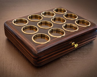 May include: A wooden box with a gold key and 12 circular compartments lined with gold trim. The box is made of dark wood with a striped pattern.