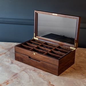 May include: A dark wood box with a glass top and a drawer. The box has 12 compartments for storing glasses.