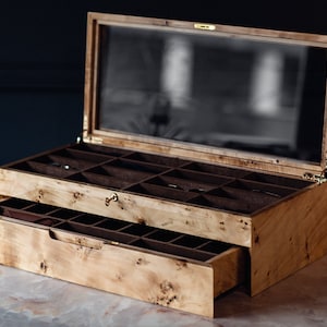 以下が含まれることがあります： ガラスの蓋と引き出しが付いた木製の箱。箱は茶色の内装で、仕切りがあります。引き出しが開いており、茶色の内装です。