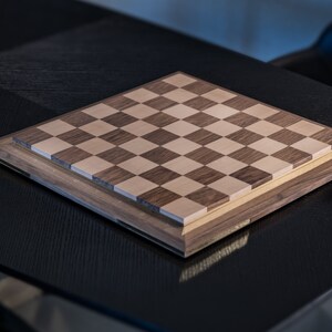 May include: A wooden chessboard with a light brown and dark brown checkered pattern. The board is on a black surface.