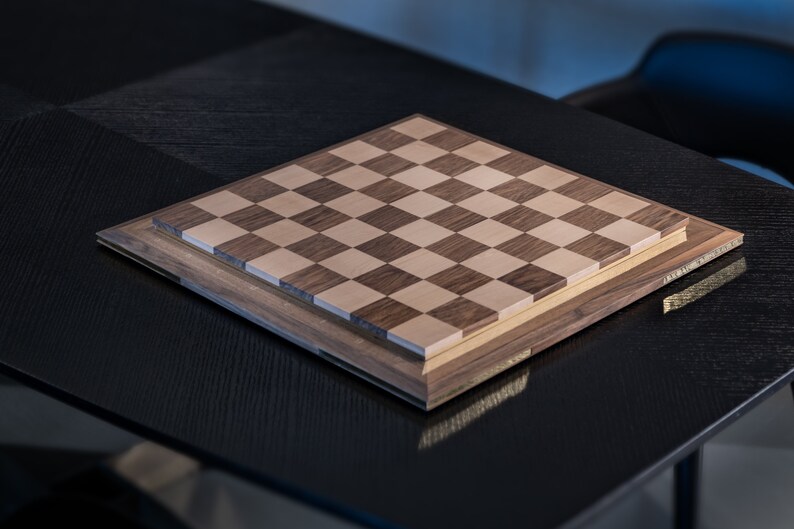 May include: A wooden chessboard with a light brown and dark brown checkered pattern. The board is on a black surface.