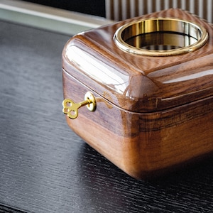 May include: A wooden music box with a gold key and a brass ring around the top. The box is closed and has a dark wood finish.
