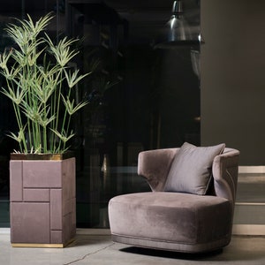May include: A plush, gray swivel chair with a gray pillow sits in a modern living room setting. A tall, leafy plant in a textured, purple planter with gold trim is next to the chair.