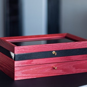 May include: A red wooden box with a glass top, a black leather drawer, and a smaller red wooden drawer with a gold knob. The box has a gold keyhole.