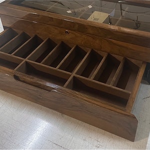 May include: A wooden box with a glass top and a drawer with multiple compartments. The drawer is open and the compartments are visible. The box is made of dark wood with a glossy finish.