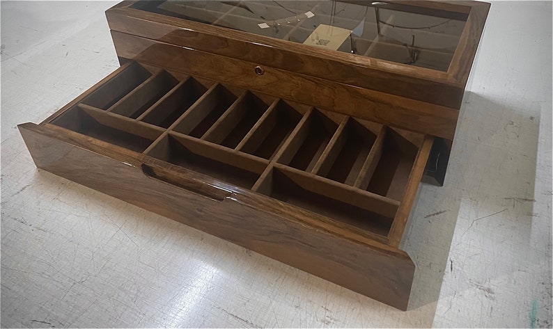 May include: A wooden box with a glass top and a drawer with multiple compartments. The drawer is open and the compartments are visible. The box is made of dark wood with a glossy finish.
