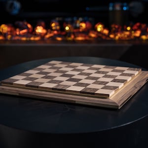 May include: A wooden chessboard with a dark brown and light wood finish. The board is sitting on a black table.