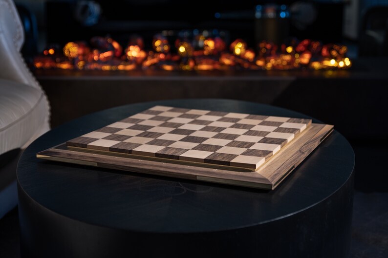 May include: A wooden chessboard with a dark brown and light wood finish. The board is sitting on a black table.