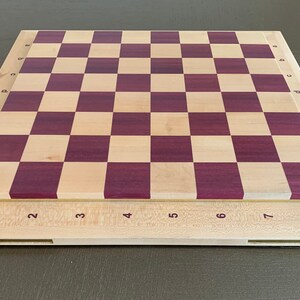 Puede incluir: Un tablero de ajedrez de madera con un marco de madera clara y una superficie de juego de madera oscura. El tablero est&aacute; numerado del 1 al 8 en cada lado y con letras de la a a la h en cada lado.