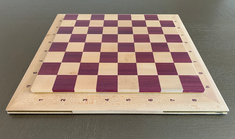 Puede incluir: Un tablero de ajedrez de madera con un marco de madera clara y una superficie de juego de madera oscura. El tablero est&aacute; numerado del 1 al 8 en cada lado y con letras de la a a la h en cada lado.