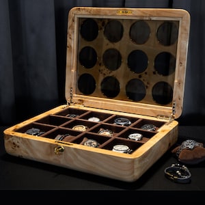 May include: A wooden watch box with a glass top and 12 compartments for storing watches. The box is open and has several watches inside.