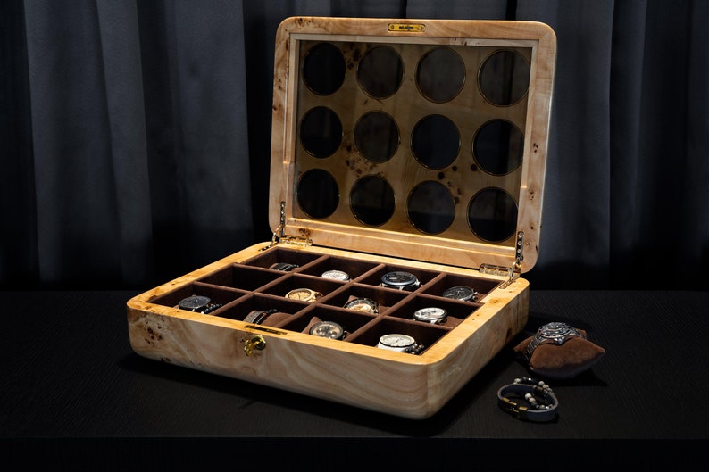 May include: A wooden watch box with a glass top and 12 compartments for storing watches. The box is open and has several watches inside.