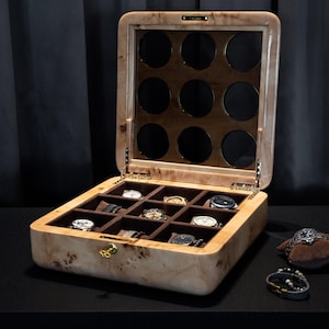 May include: A wooden watch box with a glass top and 12 compartments for storing watches. The box is made of light wood with a brown stain and has a gold-colored lock. The box is open and there are watches in some of the compartments.