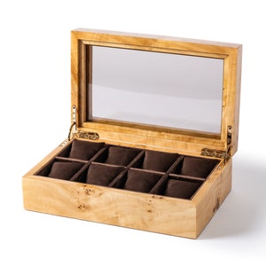 Pu&ograve; includere: Una scatola porta orologi in legno con un coperchio in vetro e otto scomparti rivestiti in velluto marrone. La scatola &egrave; aperta e gli scomparti sono vuoti.