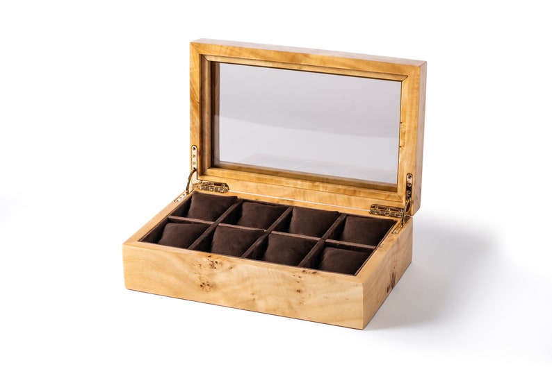Pu&ograve; includere: Una scatola porta orologi in legno con un coperchio in vetro e otto scomparti rivestiti in velluto marrone. La scatola &egrave; aperta e gli scomparti sono vuoti.