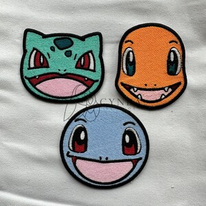 May include: Three embroidered iron-on patches featuring the faces of popular Pokemon characters: Bulbasaur, Charmander, and Squirtle. The patches are circular and have a black outline.