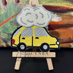 May include: A yellow car with a gray cloud on top. The car has black wheels and a red detail on the side. The cloud is white with gray shading. The image is a close-up of the car and cloud.