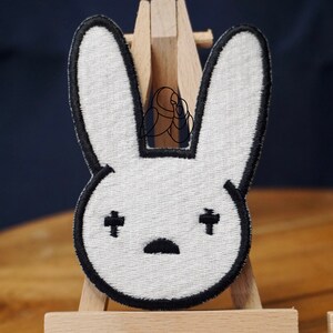 May include: White bunny rabbit patch with black outline and embroidered eyes and mouth. The patch is on a wooden easel.